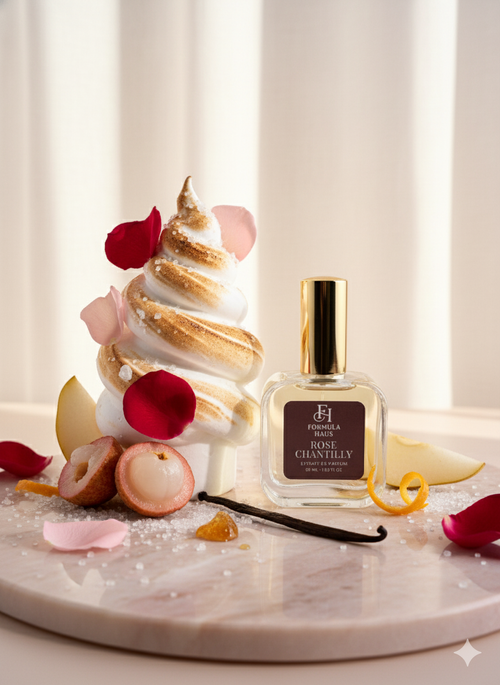 Formula Haus Rose Chantilly perfume bottle on a marble surface next to a meringue dessert topped with rose petals, lychee fruit, and vanilla bean