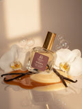 Formula haus whispa perfume bottle with vanilla beans and orchids on a reflective surface.